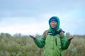 Yakut Asian girl tourist in a jacket hat, hood and glasses, with a backpack is smiling, hail and rain and snow holding up his hand