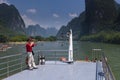 Chinese man in a boat cruising in the Li River and photographing the the tall limestone mountains near Yangshuo in China