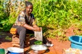 Yaounde, Cameroon - 10 august 2018: young healthy and smiling african woman doing house chores outdoor washing dishes in sunny day