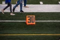 30 yard line marker on football field as feet and legs of teenagers walk past on field