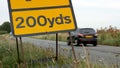 200 yards roadworks warning sign on UK motorway at evening with traffic passing Royalty Free Stock Photo