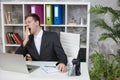 Yawing handsome man manager sitting at working place in office looking tired at the end of day. multitasking, work concept Royalty Free Stock Photo