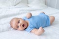 Yawning baby boy three months old in a blue bodysuit on a white bed at home goes to bed Royalty Free Stock Photo