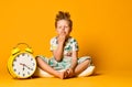 Boy in pajamas holding a toy dinosaur in his hands, sitting on a pillow with an alarm clock. Royalty Free Stock Photo