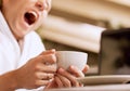 Yawning sleepy man with cup of coffee in hand