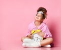 Yawning teenage girl holding an alarm clock while sitting in a housecoat on the floor.