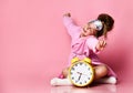 Yawning teenage girl holding an alarm clock while sitting in a housecoat on the floor.