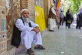 Bearded Muslim in Islamic dress is resting on city street.