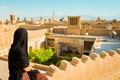 Yazd, iran - June 3rd, 2022: Iranian muslim woman wearing abaya in rooftop cafe enjoy sightseeing rooftops panorama with wind-