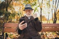 Yeah october sunny weather. White grey hair old man rest relax fall town park sit bench use smartphone check internet Royalty Free Stock Photo