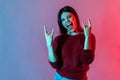 Yeah, that`s crazy! Neon light portrait of delighted happy woman showing rock and roll hand gesture, punk sign Royalty Free Stock Photo