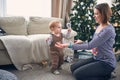 1 year old baby boy standing on the floor near his mother. the first steps concept. christmas decorations on a background Royalty Free Stock Photo