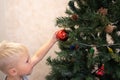A 5 year old blonde boy decorates a Christmas tree in a homely atmosphere. Festive mood. Home comfort. Life style