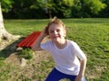 A 7-year-old boy with blond hair in a white T-shirt and blue pants poses in a city park. Child fooling around, squatting and