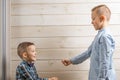 A 4-year-old boy in a blue klepy shirt cries on a light wooden background and his brother, 10 years old, is standing