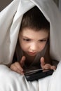 A 5 year old boy plays games on his phone while lying in bed. Gadgets in bed before bedtime in a child Royalty Free Stock Photo