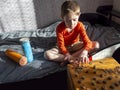 5-year-old boy puts euro cent in palm,sits on bed,selfmade jar banks near him,wooden box with scattered coin columns