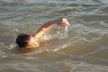 A 10-year-old boy is swimming and having fun in the sea near the shore in green swimming goggles