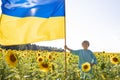 7-year-old boy with a yellow-blue large Ukrainian flag stands among a blooming field of sunflowers