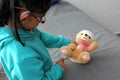 4-year-old brunette Latina girl with glasses represents mistreatment and physical abuse in her teddy bear with bandages on her hea