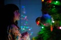 A 4-year-old charming little girl decorates a Christmas tree in light of garlands Royalty Free Stock Photo