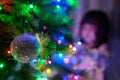 A 4-year-old charming little girl decorates a Christmas tree in light of garlands Royalty Free Stock Photo