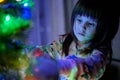 A 4-year-old charming little girl decorates a Christmas tree in light of garlands Royalty Free Stock Photo