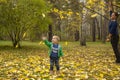 A 5 year old child rejoices at the yellow leaves falling from a tree.