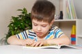 A 4-year-old child sits at a table and reads a book, looks at pictures, learns to read.