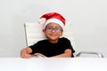 6 year old dark latino boy is ready to celebrate the holidays and write his letter to Santa Claus with Christmas hat