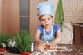 5 year old girl in blue dress and dressed as chef in kitchen laughs and rolling out dough Royalty Free Stock Photo