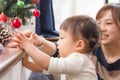 1-year-old girl and mother by window in living room, decorating Christmas tree Royalty Free Stock Photo