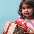 A 3-year-old girl in a red and white dress with a gift in her hands. The gift is packed in kraft paper with a red ribbon Royalty Free Stock Photo