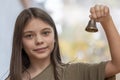 An 11-year-old girl rings a bell on a blurry neutral background.