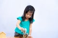 A 3-4 year old girl saves money from snack in glass jar. Child poured silver coin into jar with lid. Kid wear green shirt.