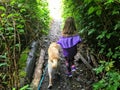 A 6 year old girl walking along a trail with her dog outside Sooke, surrounded by forest. On Vancouver Island, British Columbia