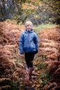 A 10 year old girl wearing wellies, on a woodland walk, surrounded by ferns.