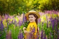 3-5-year-old girl in a yellow dress and hat on a lupine field on a sunny day. Portrait of a child with purple and lilac flowers
