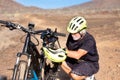 70 year old grandfather checks his electric bike. Yellow helmet Outdoor activity in arid path in the sunset light