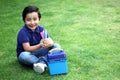 6 year old latino boy sitting on the grass with lunch box and colors for back to school