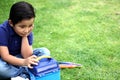 6 year old latino boy sitting on the grass with lunch box and colors for back to school