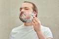 A 35-40 year old man shaves his beard with a safety razor, lifestyle