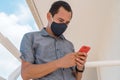 30-year-old man wearing a face mask, holding a cell phone on his balcony during the pandemic Royalty Free Stock Photo