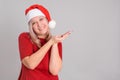 A 40-year-old middle-aged woman in a Santa Claus hat points her finger at copyspace on a gray background Royalty Free Stock Photo