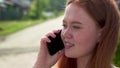 18 year old red-haired girl happily talking on the phone while standing outside on a summer day. Close-up. Royalty Free Stock Photo