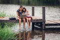 A 13-year-old sister and her 11-year-old sister sit Teach homework with a computer with an internet on a wooden bridge, The river Royalty Free Stock Photo