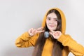 A 12-year-old teenage girl in bright clothing and a hood shows fashionable signs with her fingers. Copy the space for text