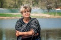 55-60-year-old woman in a knitted shawl is sitting on the riverbank. woman is resting in nature alone Royalty Free Stock Photo