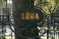 1854 Year Sign On Metal Forging Fence In Front Of Big Tree. Information Table Placard Or Signboard In Park Or Botanic Garden To