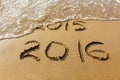 2015 and 2016 year written on sandy beach sea. Wave washes away 2015. Royalty Free Stock Photo